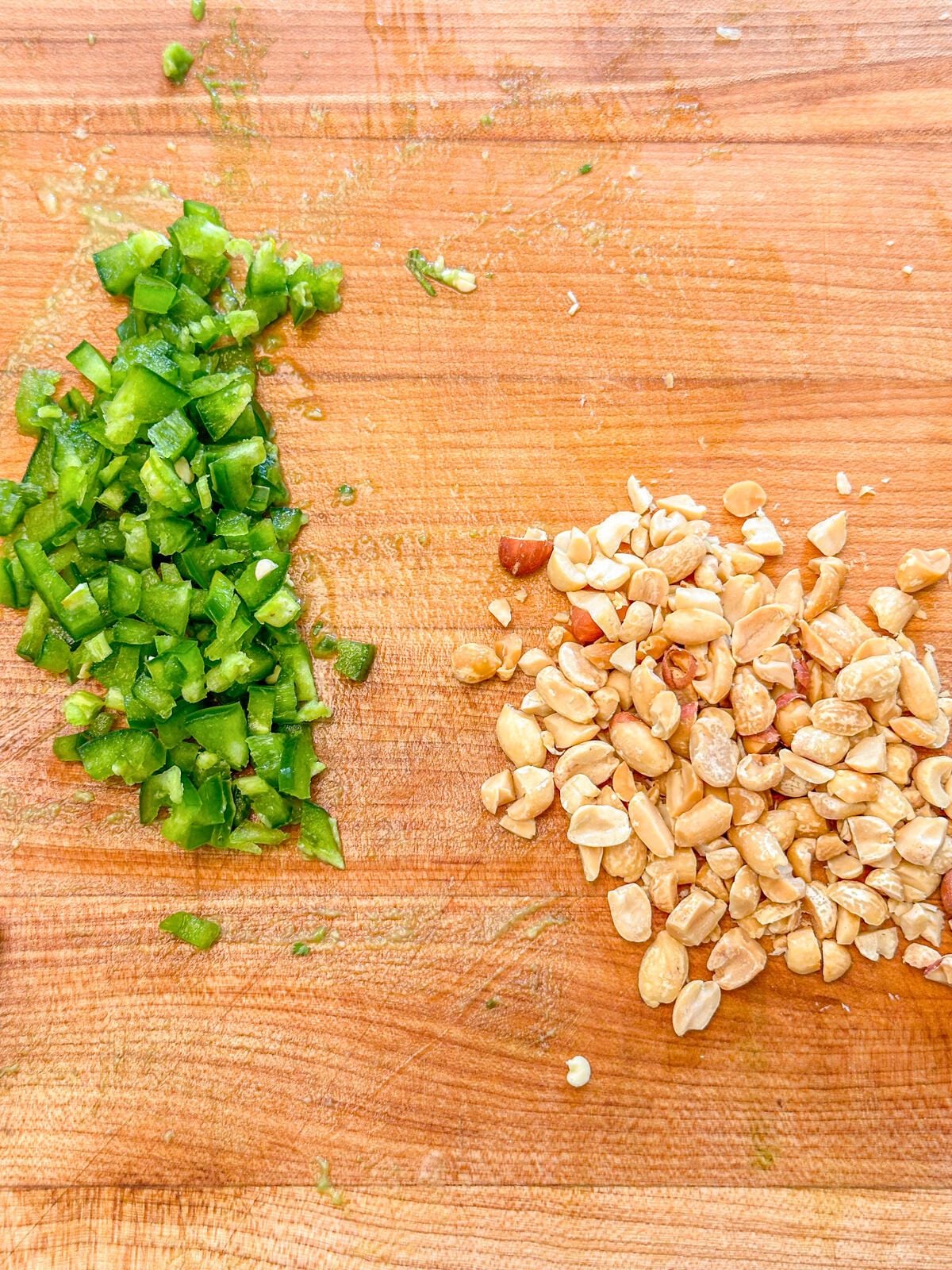 Chopped jalapeno and peanuts on a wooden chopping board.