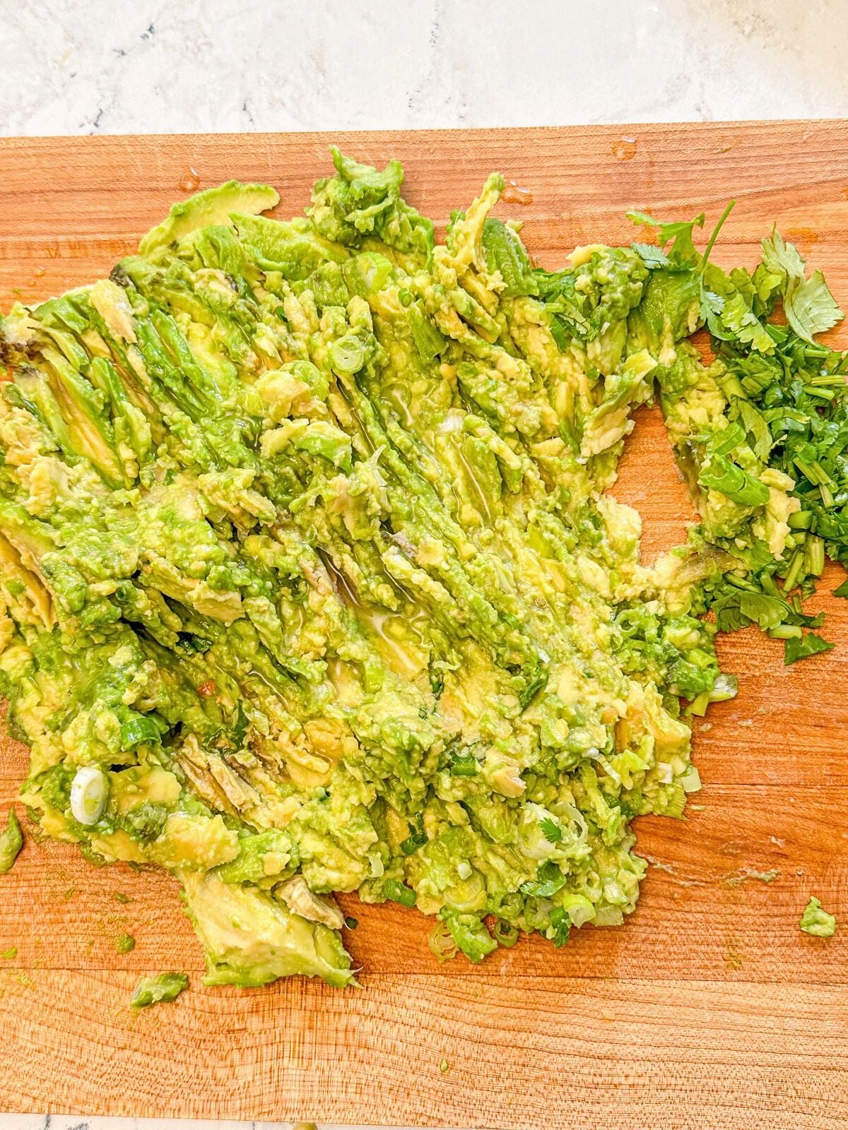 Avocado flash placed on a wooden chopping board mixed with green onions, cilantro, and jalapeno.
