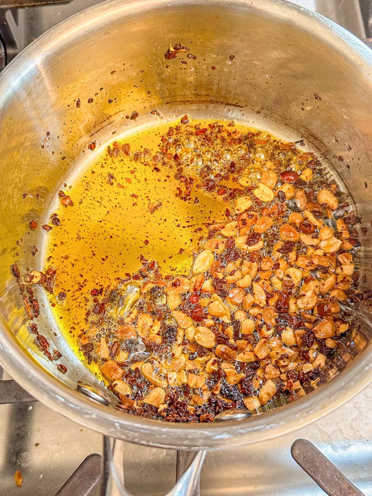 Chopped peanuts toasting in chili oil in a pot.
