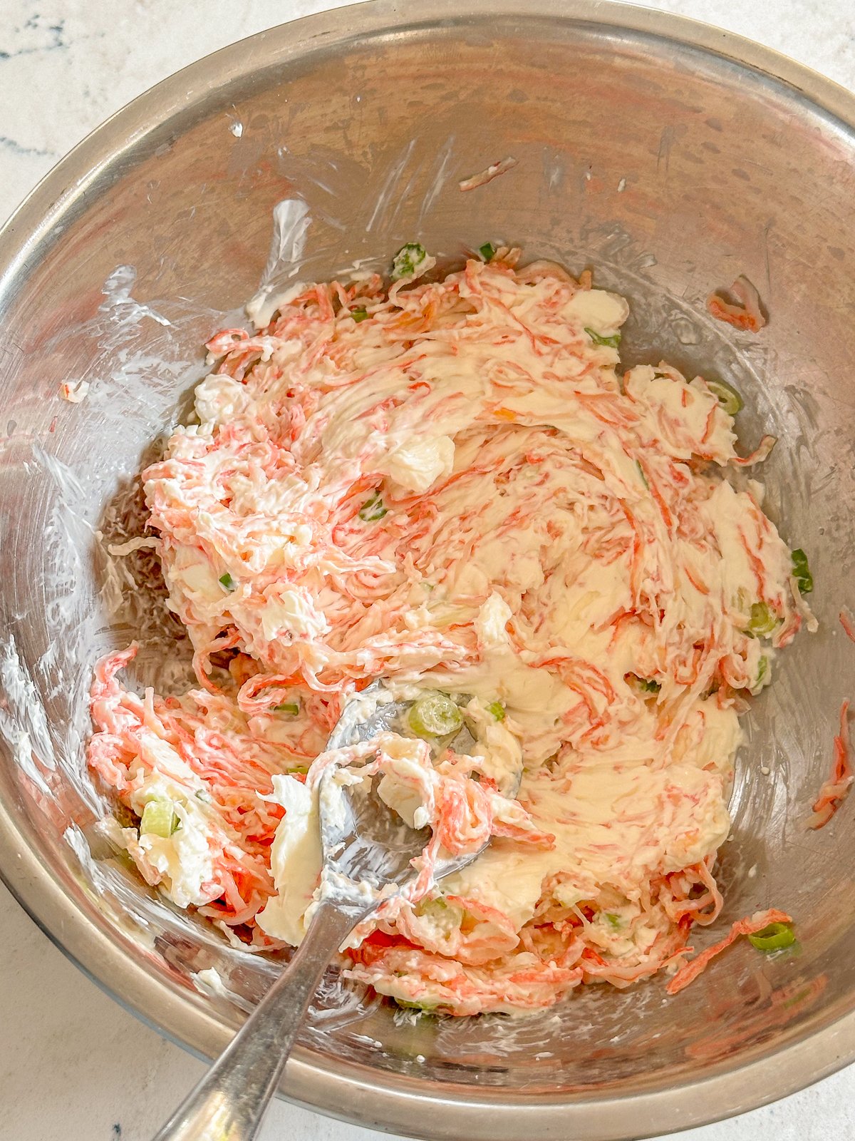 Bowl mixed with cream cheese, imitation crab, and green onions.