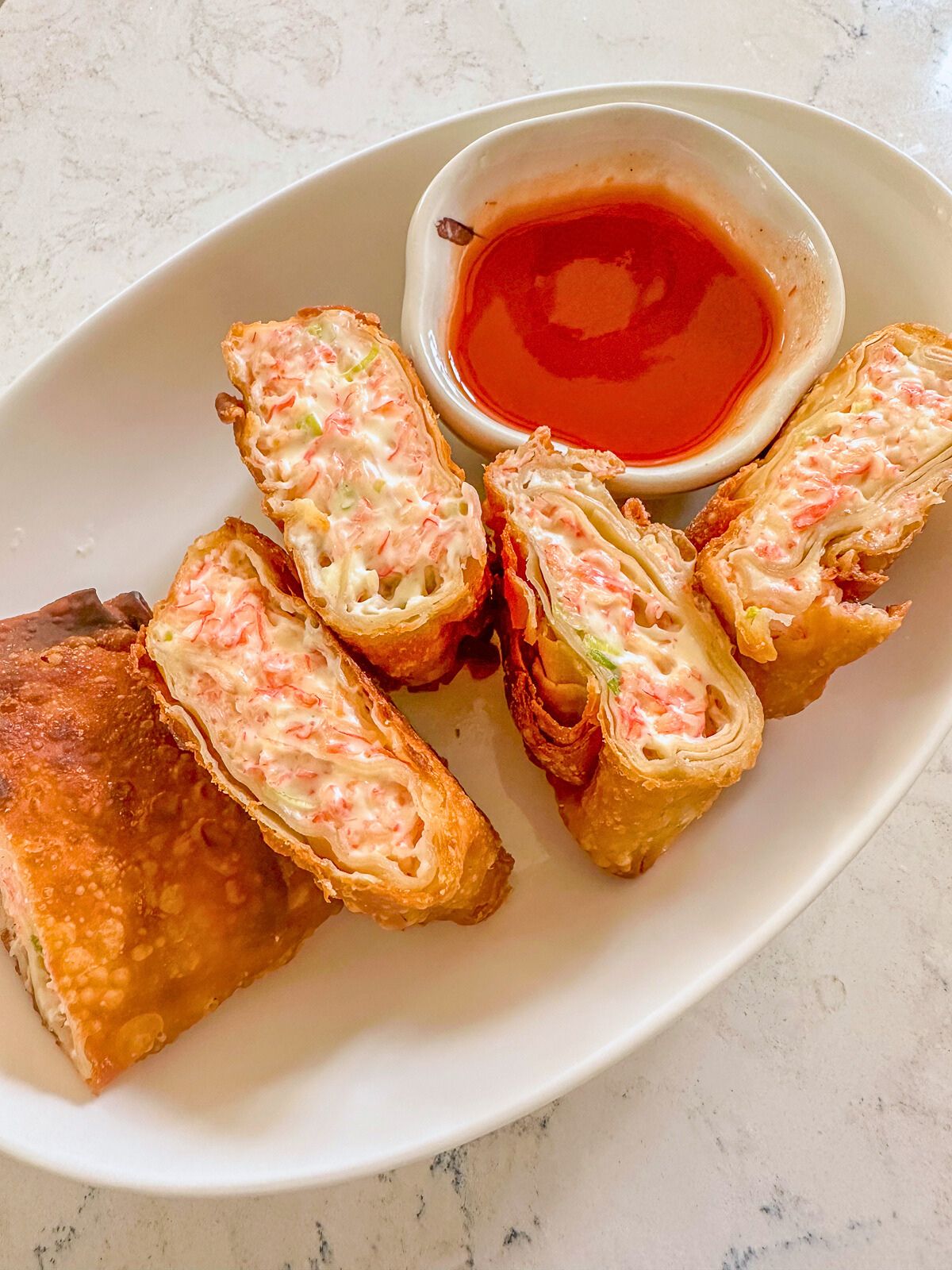 Plate of crab rangoon burrito served with sweet and sour dipping sauce on the side.