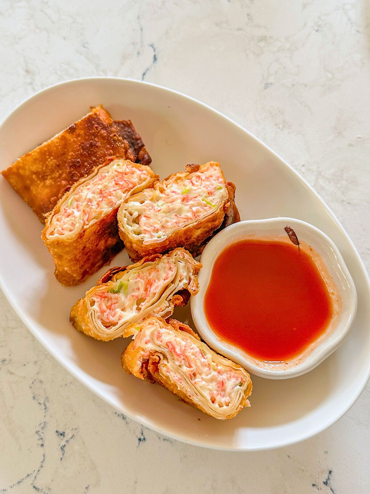 Plate of crab rangoon burrito served with sweet and sour dipping sauce on the side.