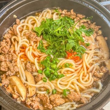 A bowl of noodle soup with ground pork and mushrooms, topped with cilantro.