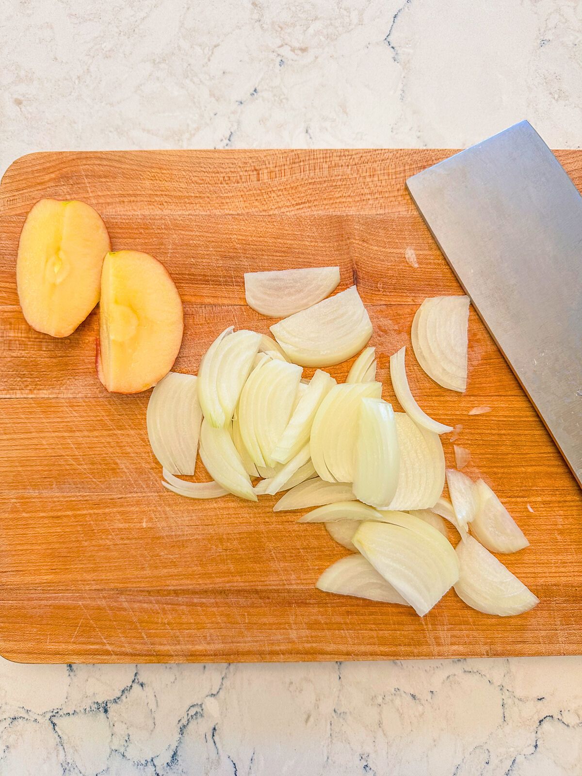 Sliced apples and white onions on a wooden chopping board.
