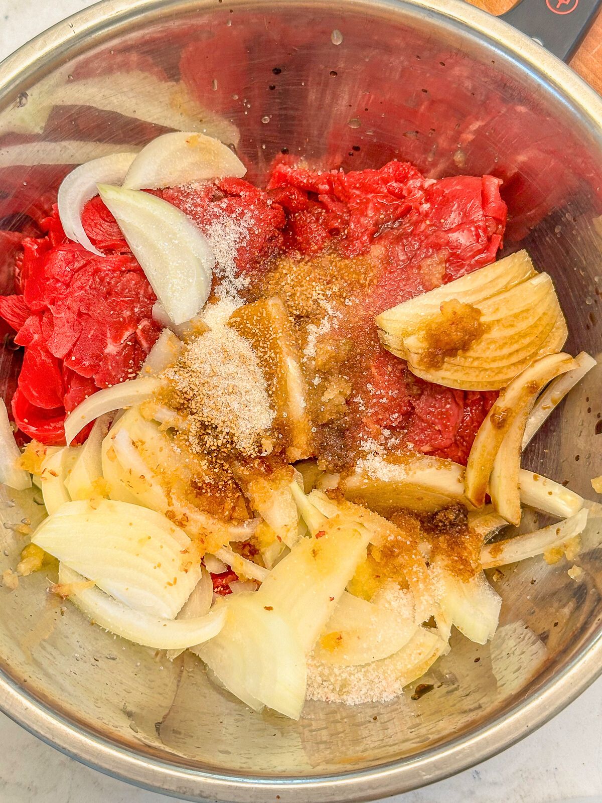 Bowl filled with sliced beef and chopped onions, topped with dashi powder, sugar, and salt.