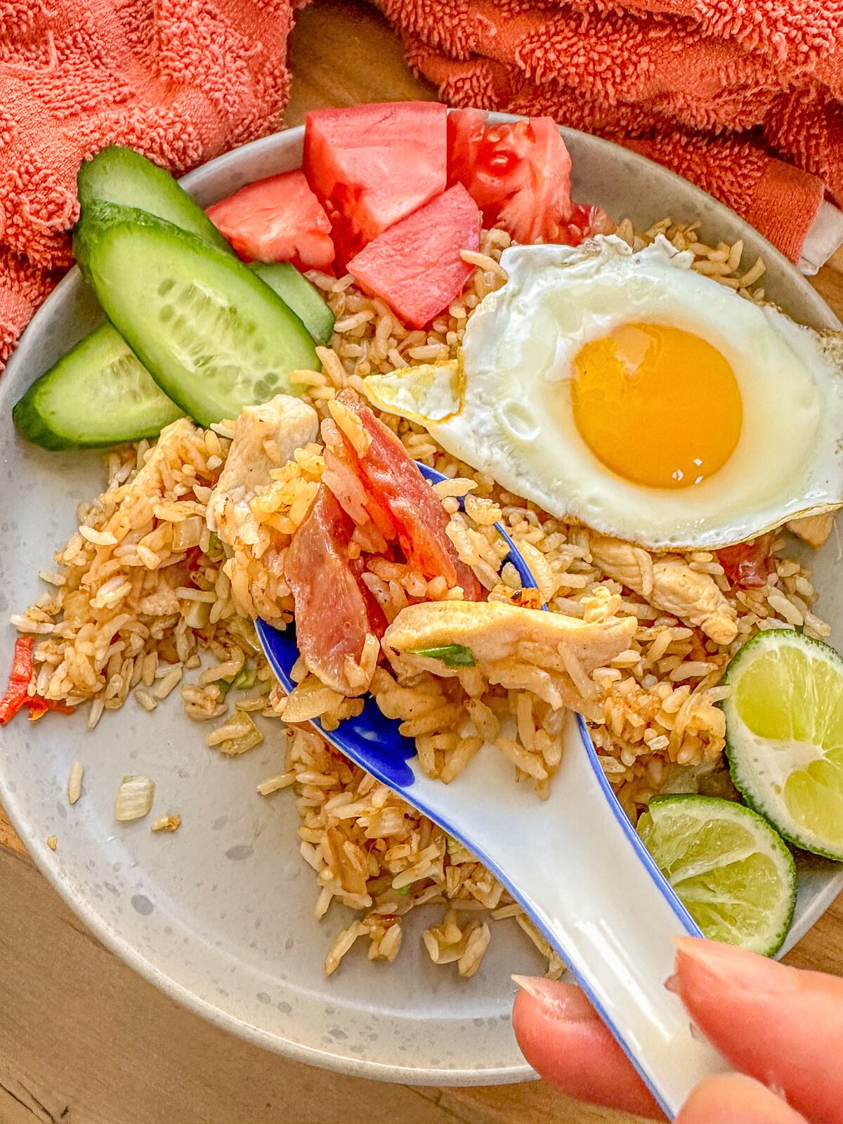 A plate of fried rice with fried egg, slices of cucumbers, tomatoes and lime on the side.