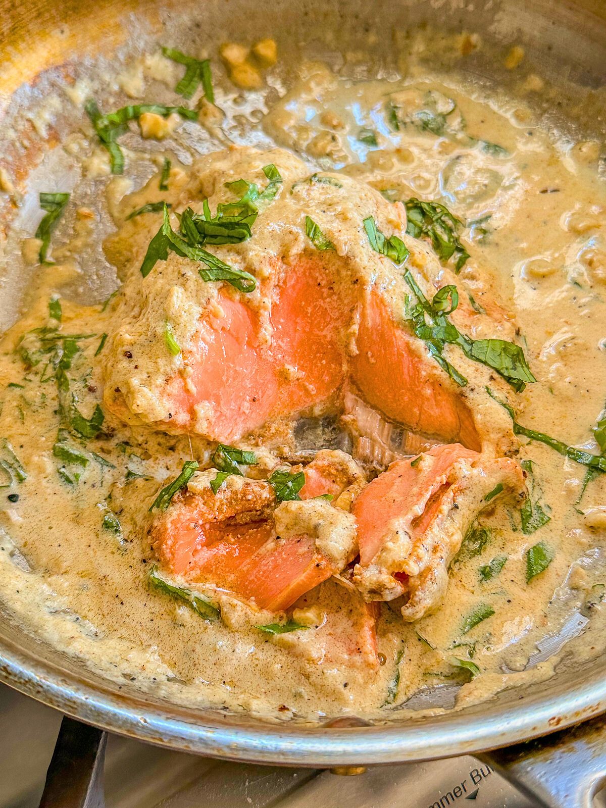 Cooked salmon coated in a creamy sauce with fresh basil in a pan.