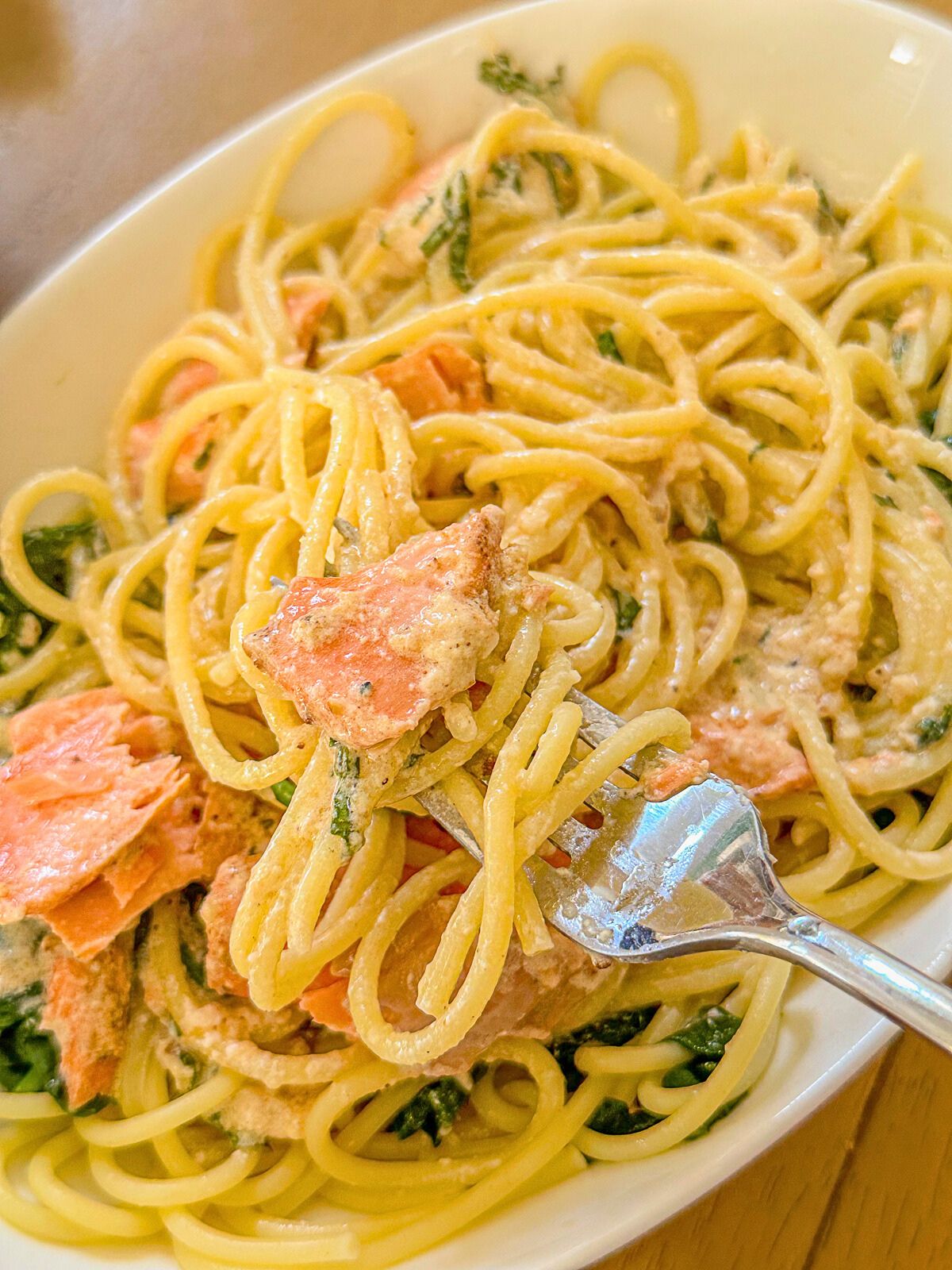 A plate of pasta coated in a rich, creamy sauce with salmon chunks and fresh basil.