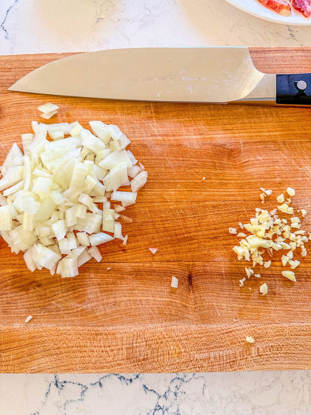 Chopped onion and garlic on a cutting board with a knife beside them.