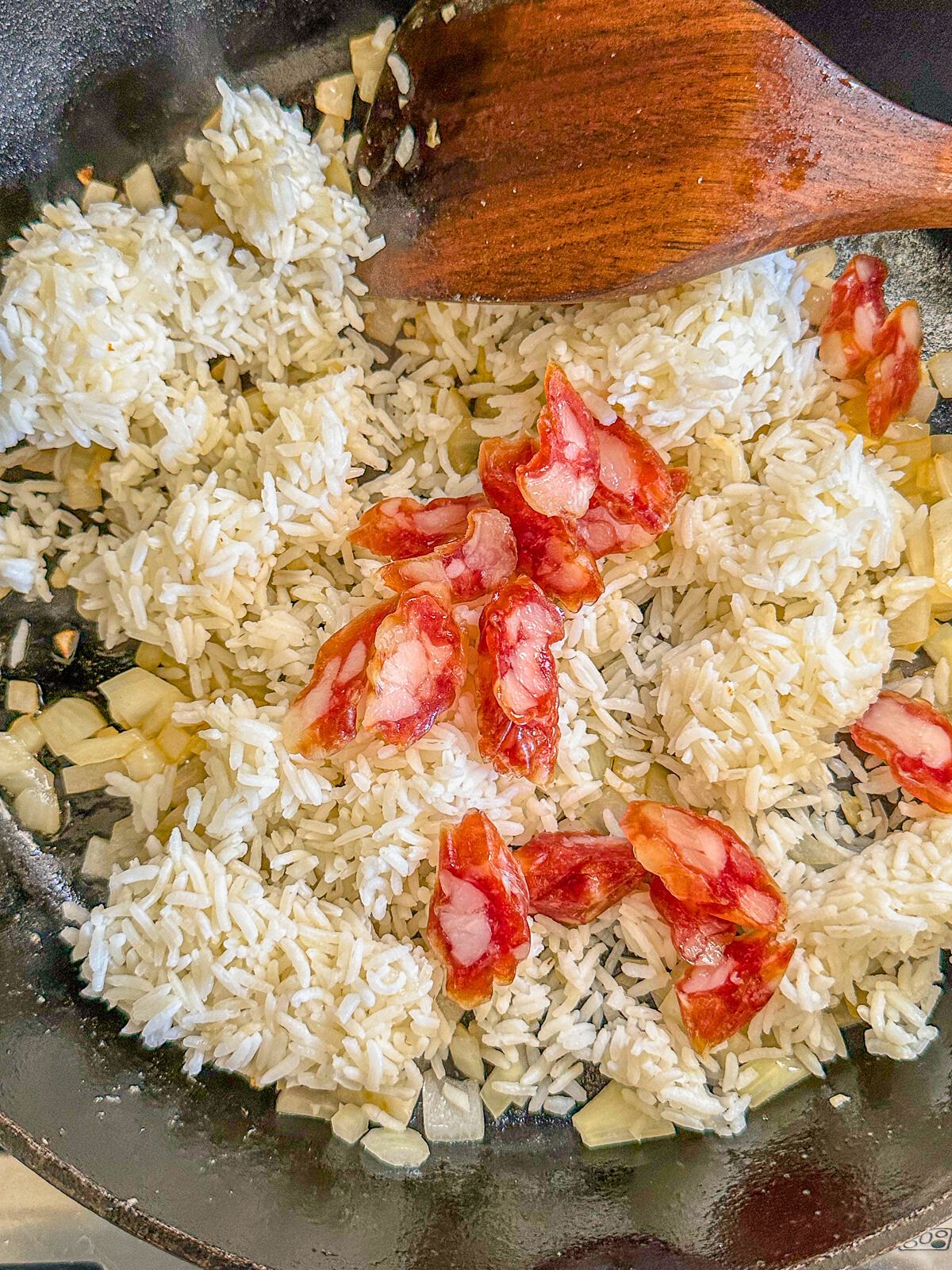 Cooked white rice with onions, garlic, and Chinese sausage in a pan.