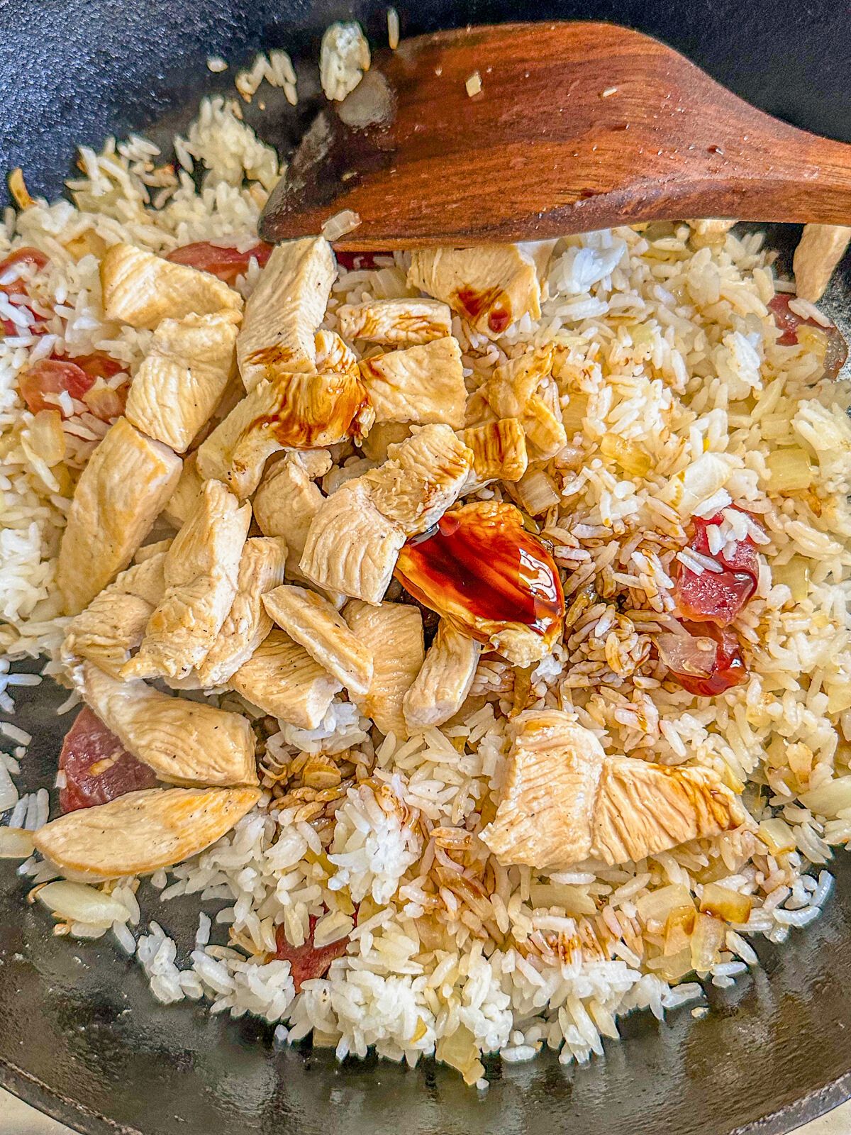 Cooked white rice with onions, garlic, Chinese sausage, and chicken, drizzled with sweet soy sauce in a pan.