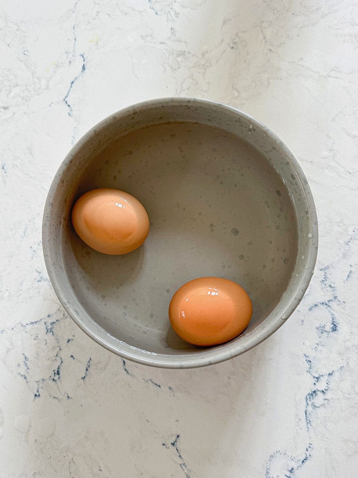 Two boiled eggs in a small bowl filled with water.