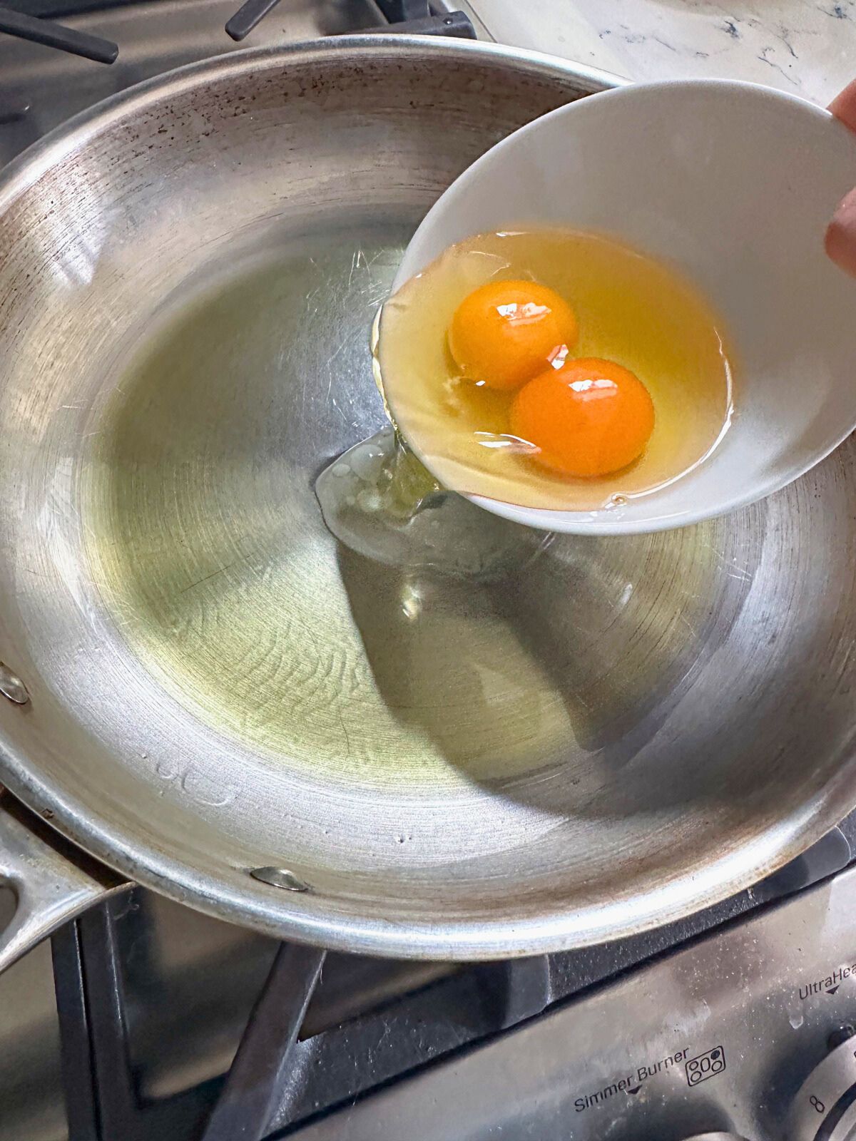 Placing two raw eggs in a pan with cooking oil.