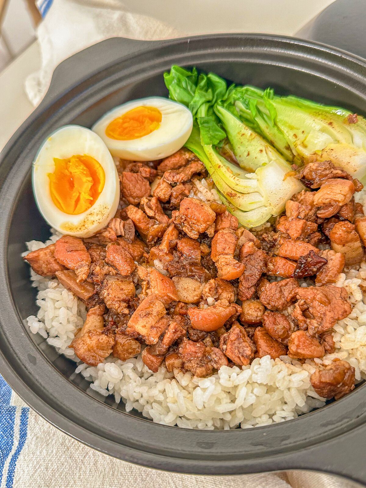 A bowl of minced pork served over rice, paired with a soft-boiled eggs and fresh bok choy on the side.
