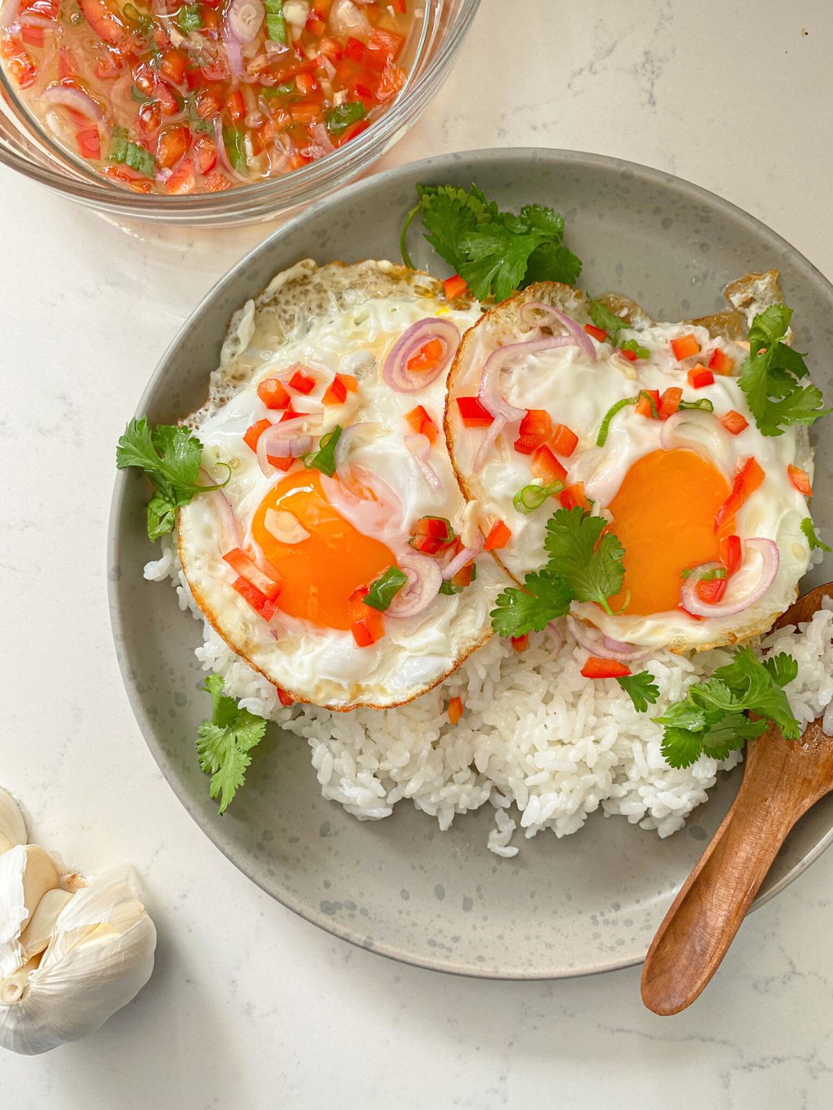 Sunny-side-up eggs over white rice, garnished with shallot, scallion, red bell pepper and cilantro served with a lime fish sauce on the side.