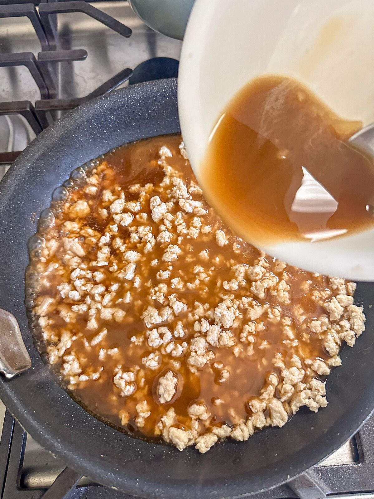 Pouring sauce over ground meat in a pan.