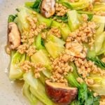 A plate of cooked bokchoy with pieces of mushroom and minced pork drenched in garlic sauce.