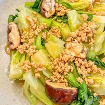 A plate of cooked bokchoy with pieces of mushroom and minced pork drenched in garlic sauce.