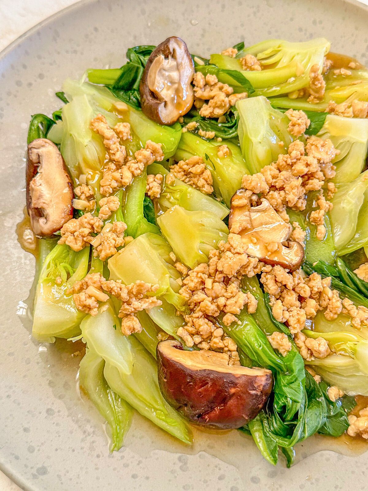 A plate of cooked bokchoy with pieces of mushroom and minced pork drenched in garlic sauce.