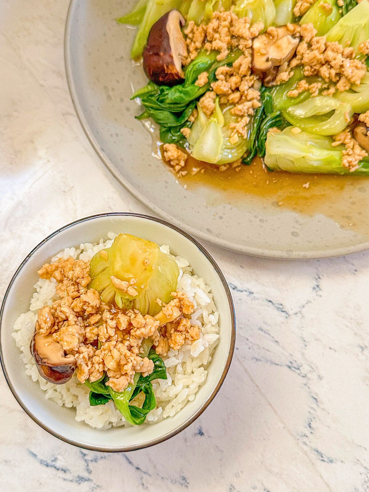 A bowl of rice with bok choy, mushrooms, and minced pork, served next to a plate of cooked bok choy.