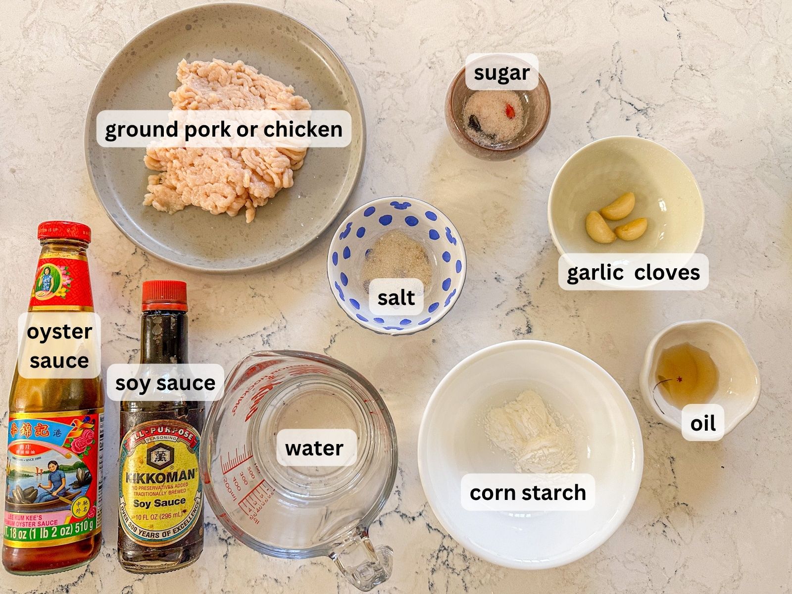 Ingredients for Bok choy with garlic sauce displayed on a surface with a plate of ground pork/chicken, sugar, salt, soy sauce, oyster sauce, water, garlic cloves, oil and corn starch.