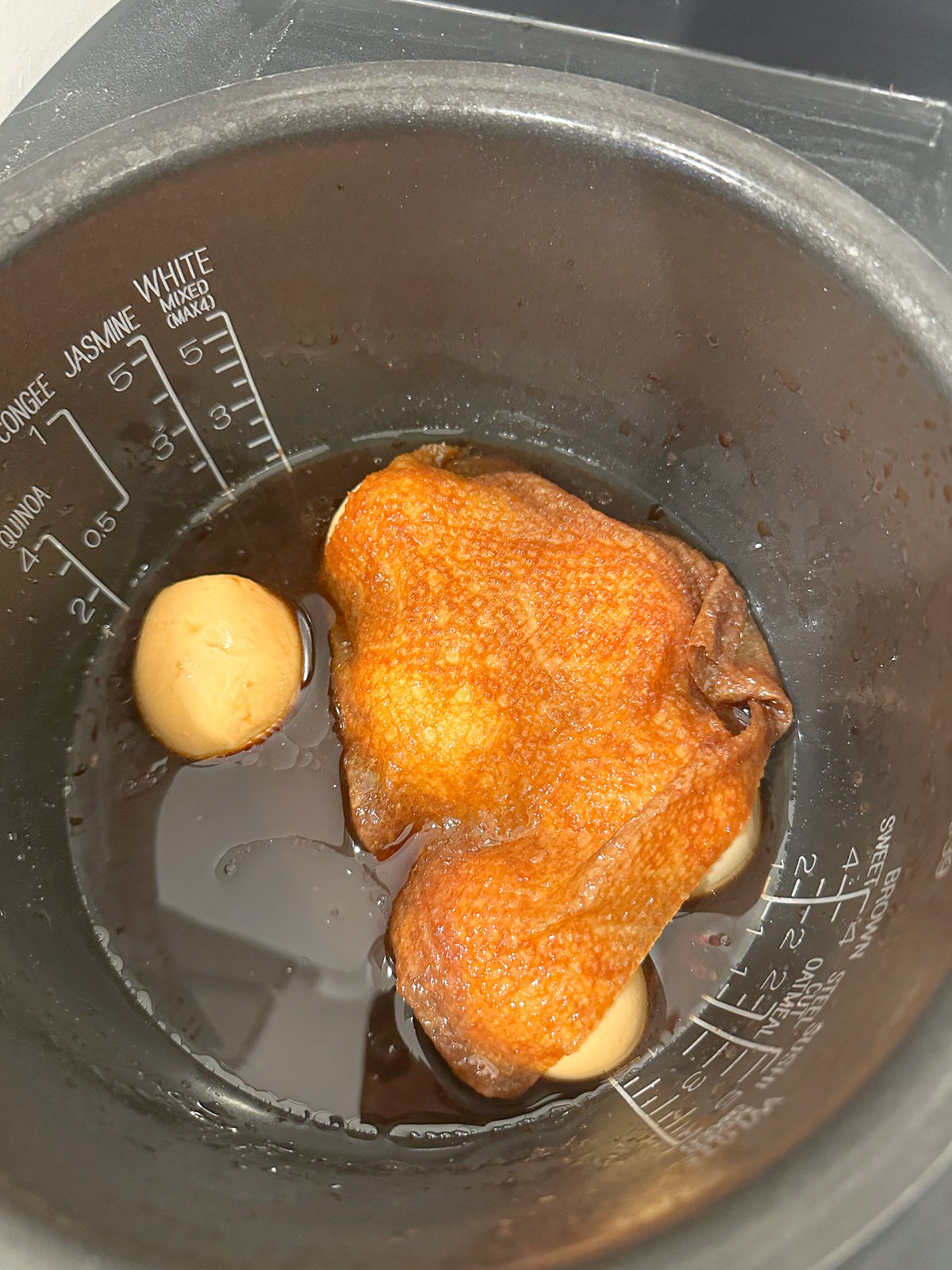 Six boiled eggs in a pot filled with soy sauce and covered with a paper towel.