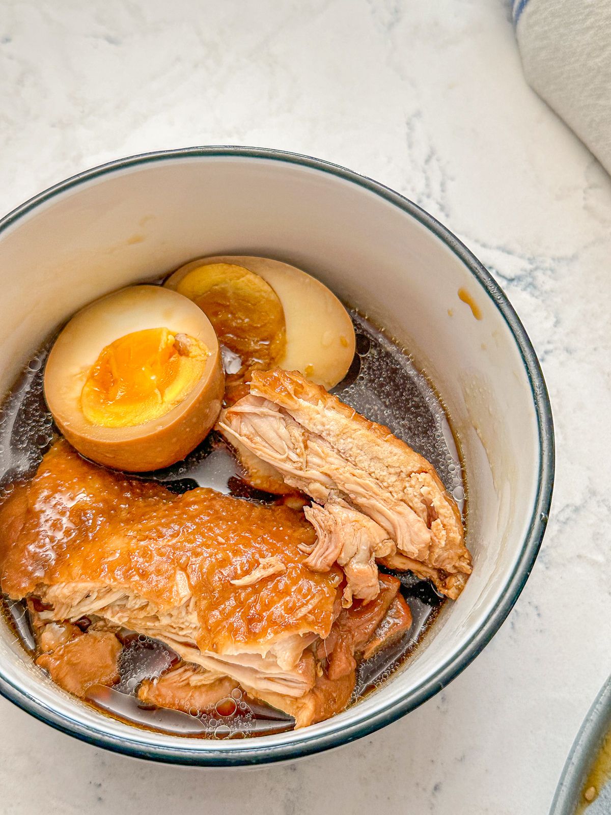 A bowl of cooked chicken served with a boiled egg and soy sauce.