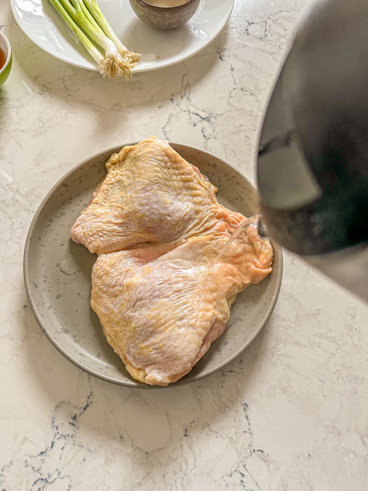 A dish of raw chicken with a pot of boiling water ready to be poured over it.