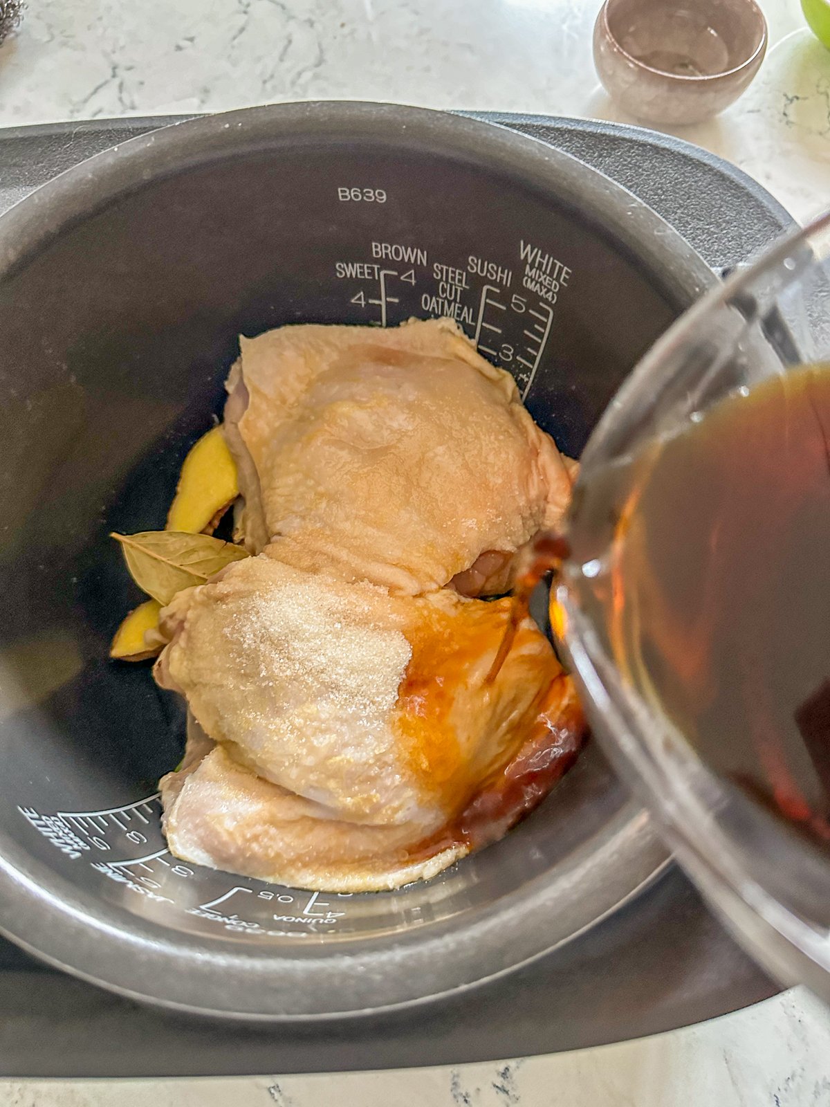 Raw chicken in a pot with a cup of sauce ready to be poured over it. 