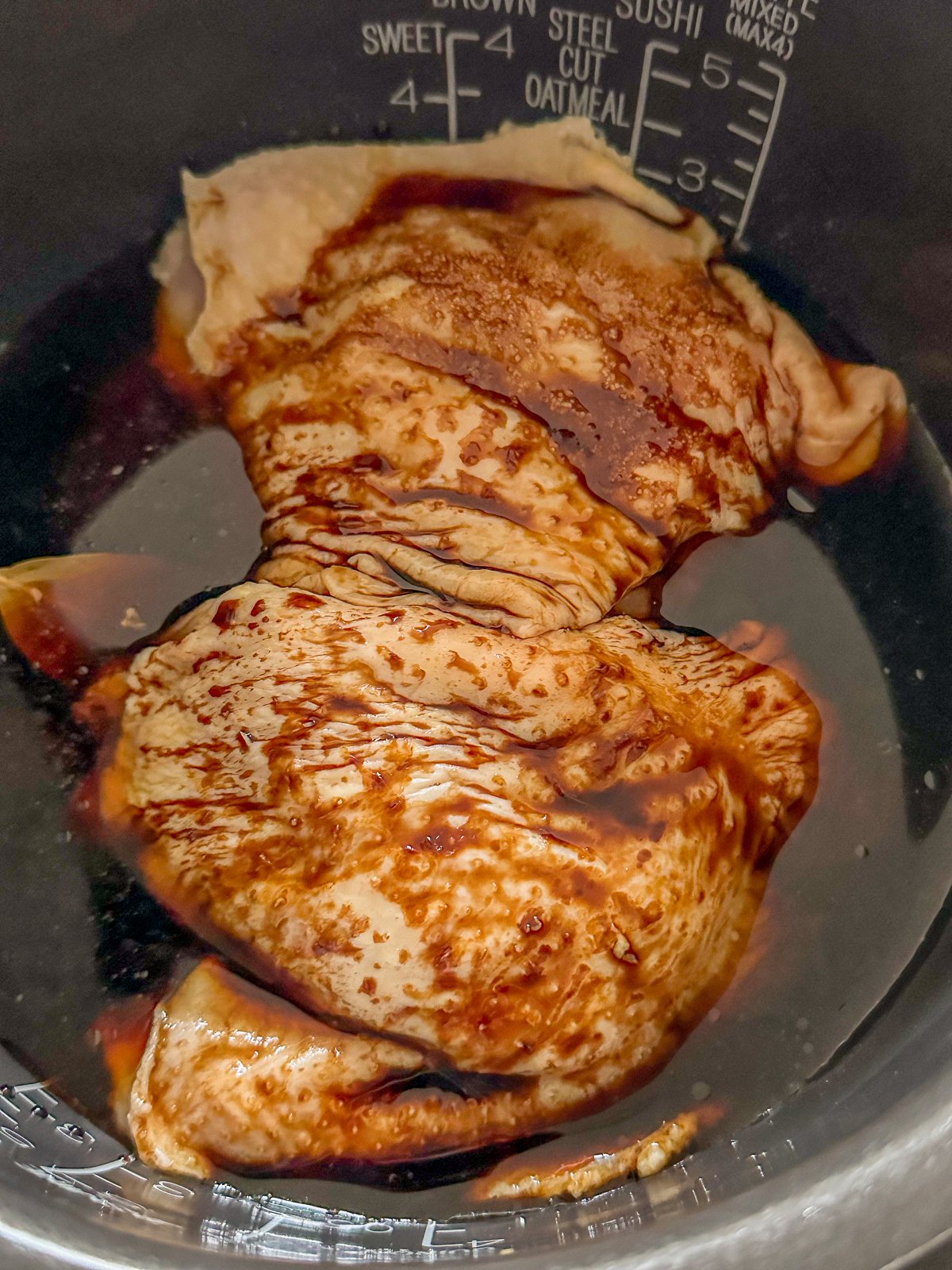 Raw chicken sitting in a pot filled with soy sauce.