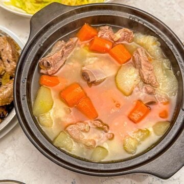 A pot of chinese pork and squash soup with chopped carrots, served alongside stir-fried cabbage, pork in black bean sauce, and rice.