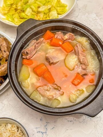 A pot of chinese pork and squash soup with chopped carrots, served alongside stir-fried cabbage, pork in black bean sauce, and rice.