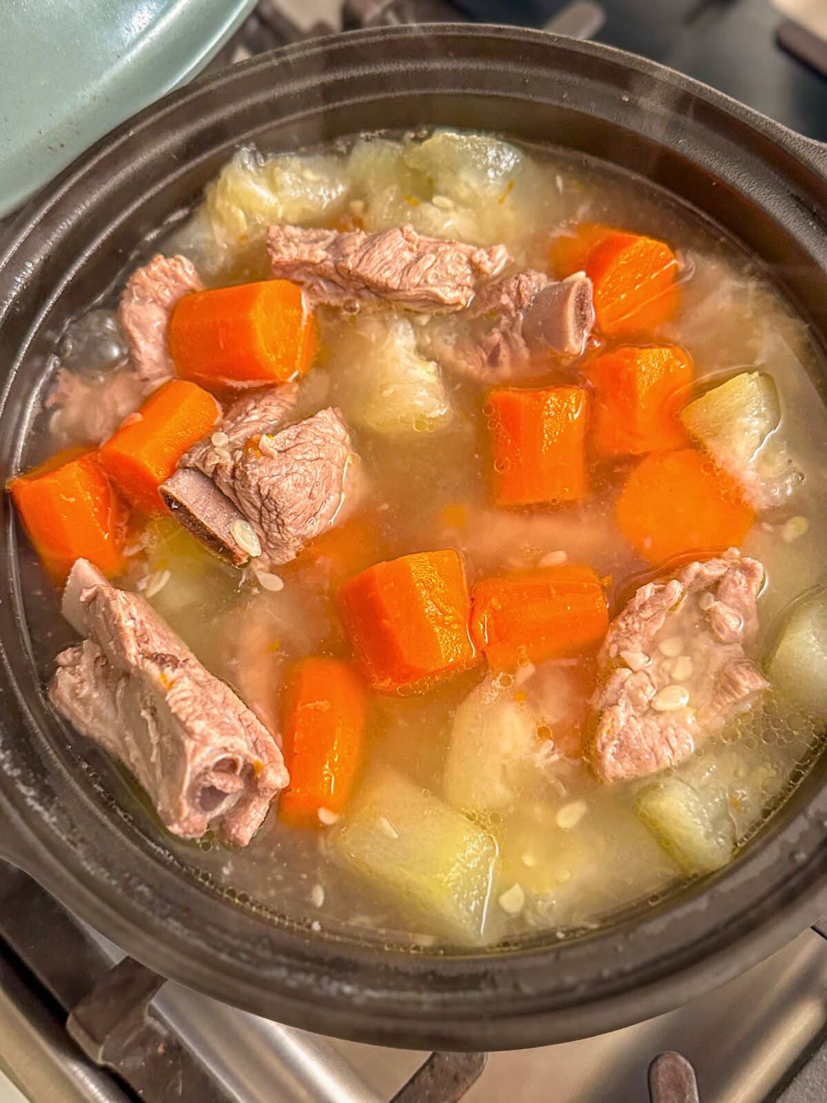 Chinese pork and squash soup with chopped carrots simmering in a black pot.