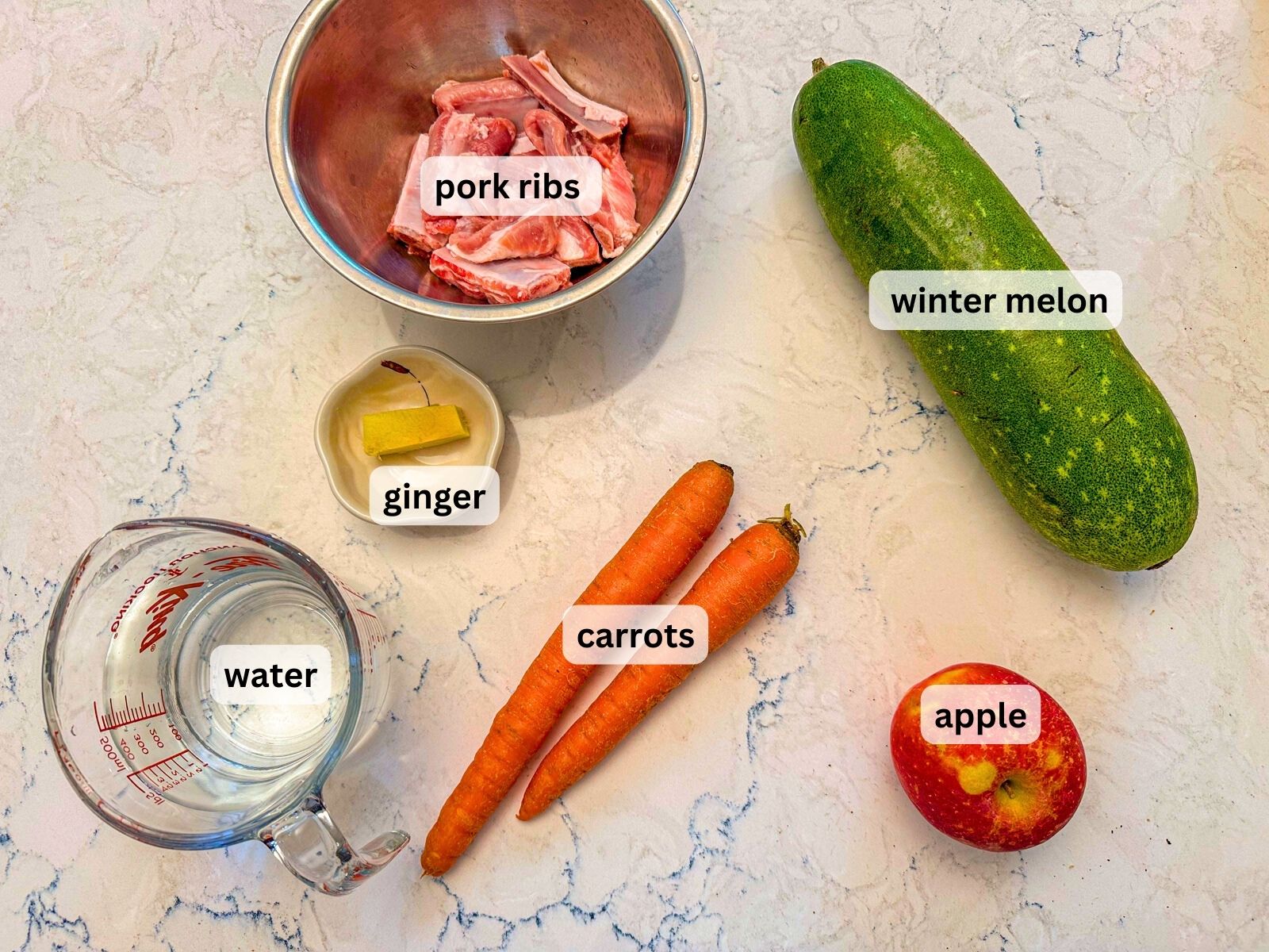 Chinese pork and squash soup ingredients laid out on the table countertop inlcuding pork ribs, wintermelon, ginger, carrots, apple and water.