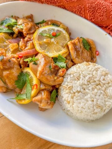A plate of cooked chicken topped with lemon slices, chopped onions, cilantro, and chilies served with white rice.