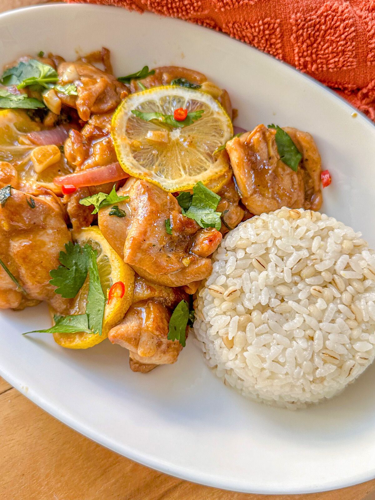 A plate of cooked chicken topped with lemon slices, chopped onions, cilantro, and chilies served with white rice.