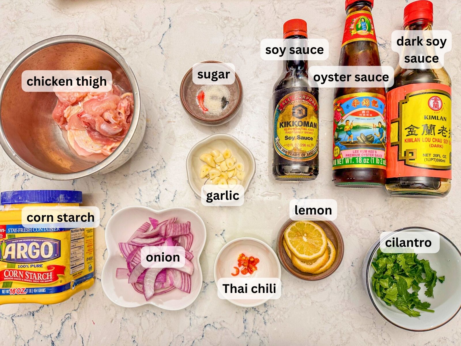 One pan lemon chicken ingredients laid out on the countertop including chicken thigh, garlic, onion, lemon, corn starch, chillies, cilantro and condiments.