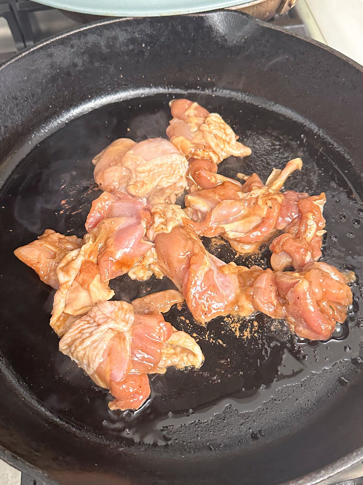 Raw chicken pieces on a pan with cooking oil.