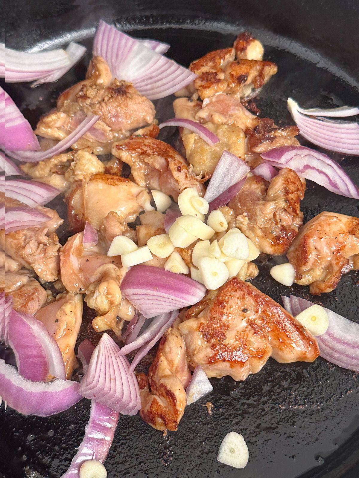 Cooking chicken with chopped onions and garlic in a pan.