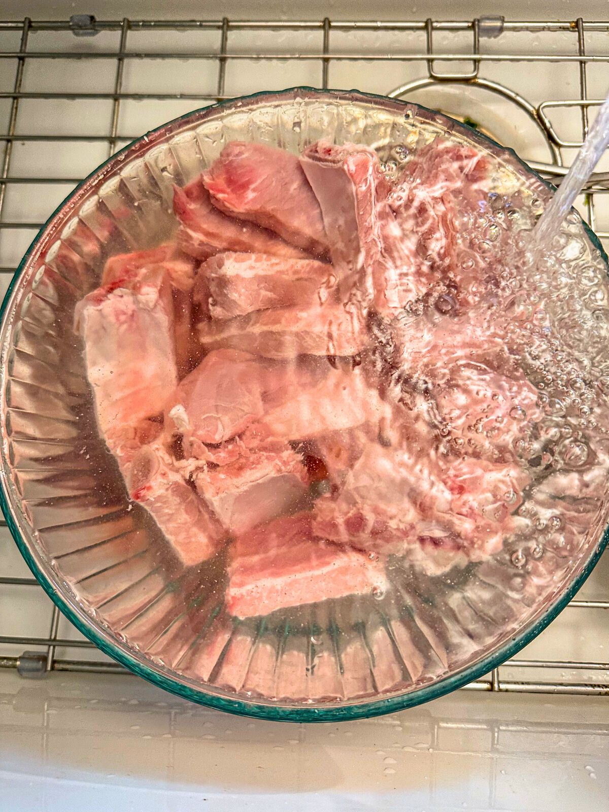 Pork ribs soaking in a bowl under running water.