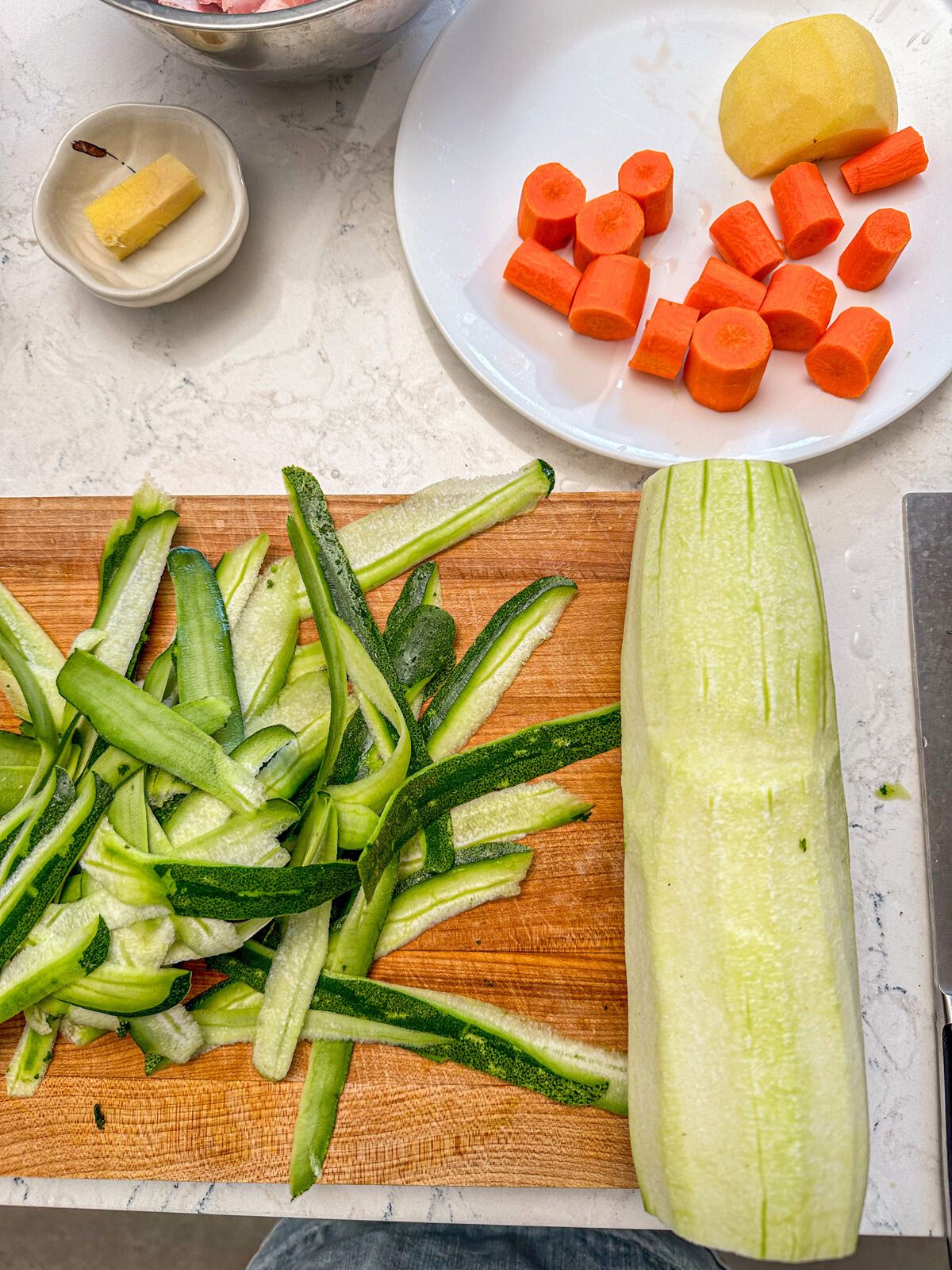 Peeled winter melon on a cutting board with a plate of chopped carrots, sliced apple and ginger beside it.