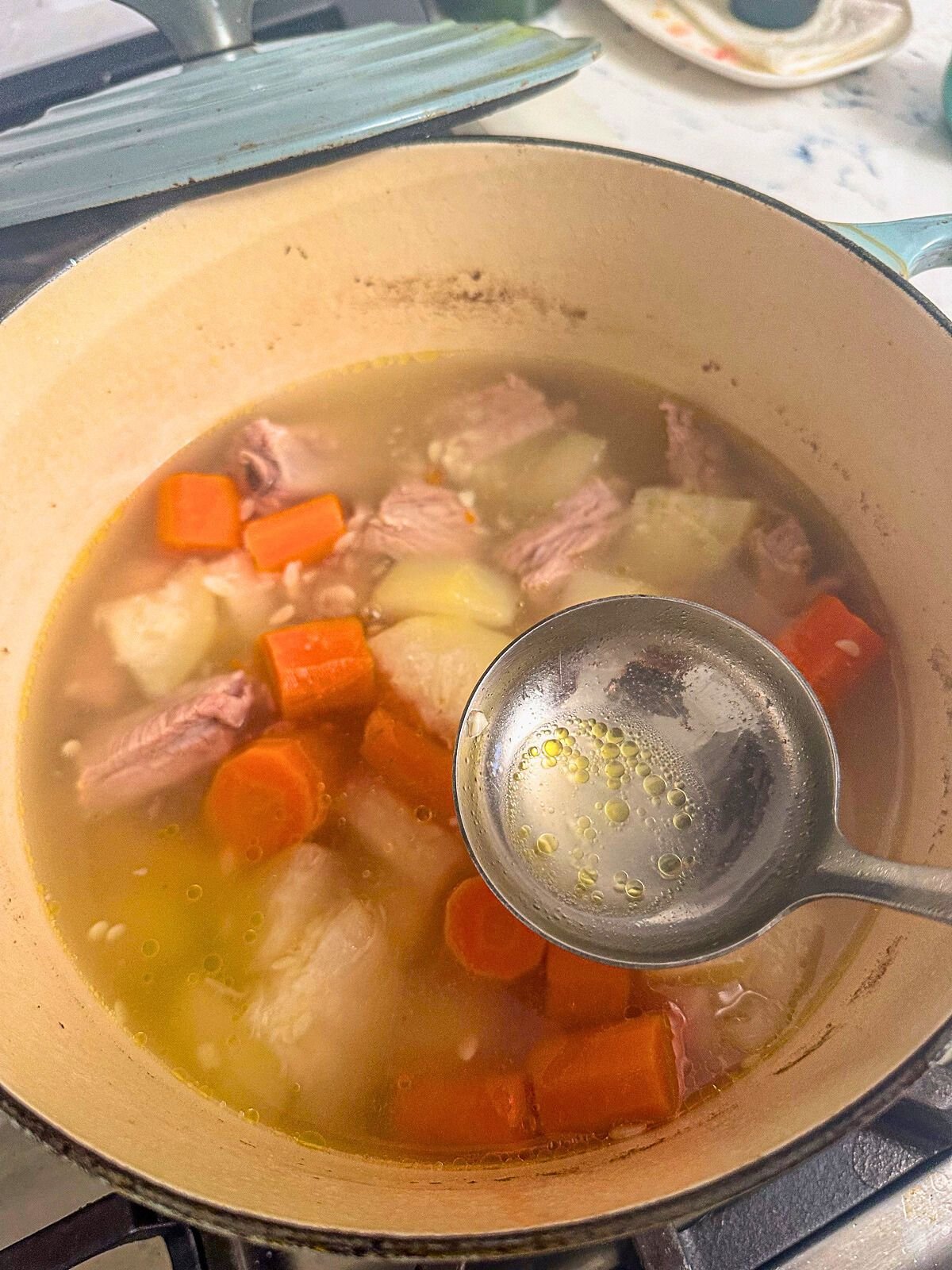 Skimming oil from a pot of simmering water with chopped winter melon, carrots, half a sliced apple, and pork ribs.