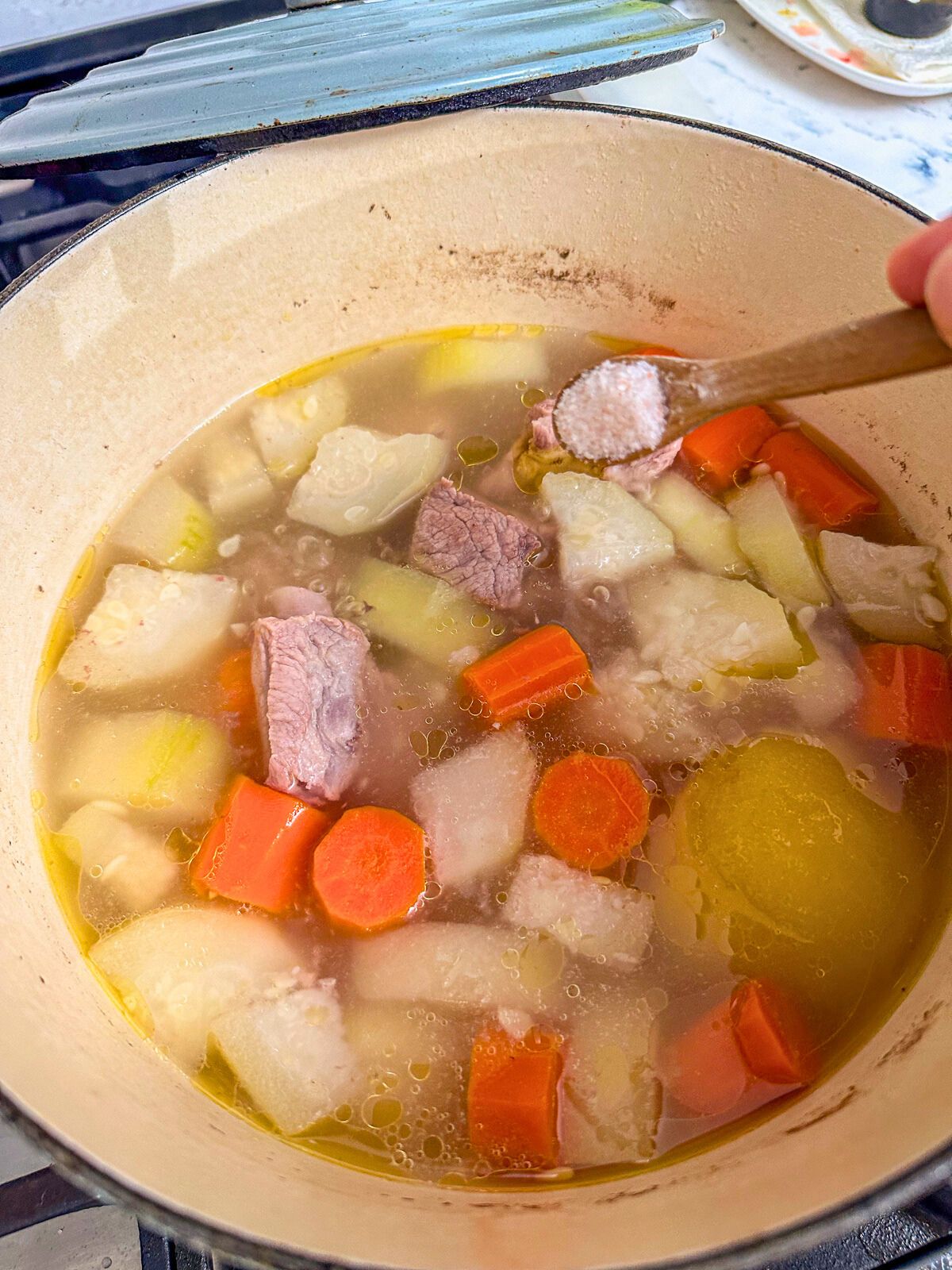 Adding a teaspon of salt in a pot of simmering water with chopped winter melon, carrots, half a sliced apple, and pork ribs.
