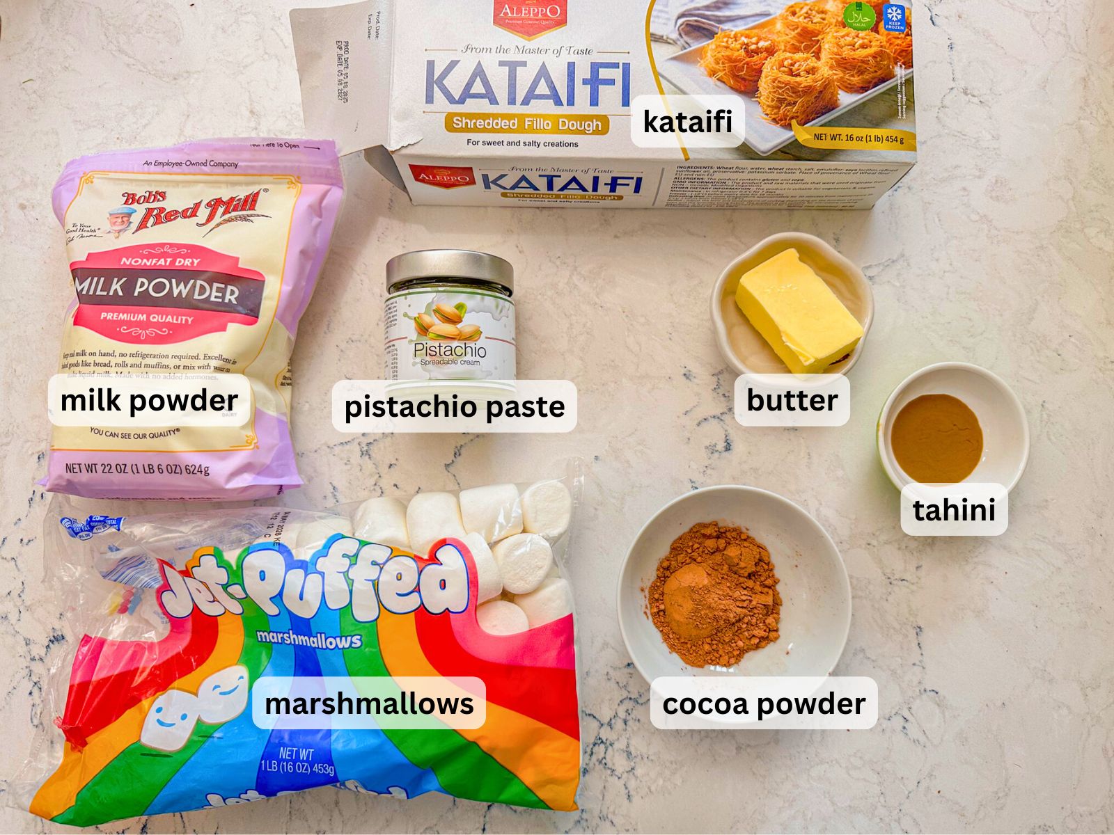 Korean Dubai chocolate chewy cookie ingredients laid out on the table countertop lincluding Kataifi, milk powder, pistachio paste, butter, tahini, marshmallows and cocoa powder.
