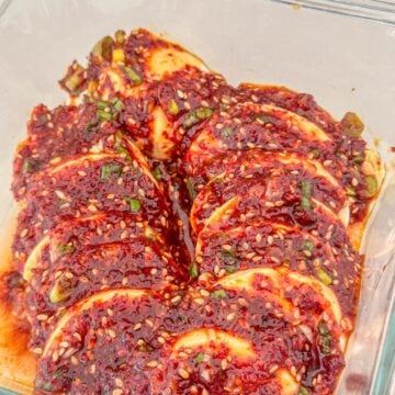 Sliced silken tofu in a spicy, savory Korean sauce with green onions and sesame seeds served in a glass bowl.