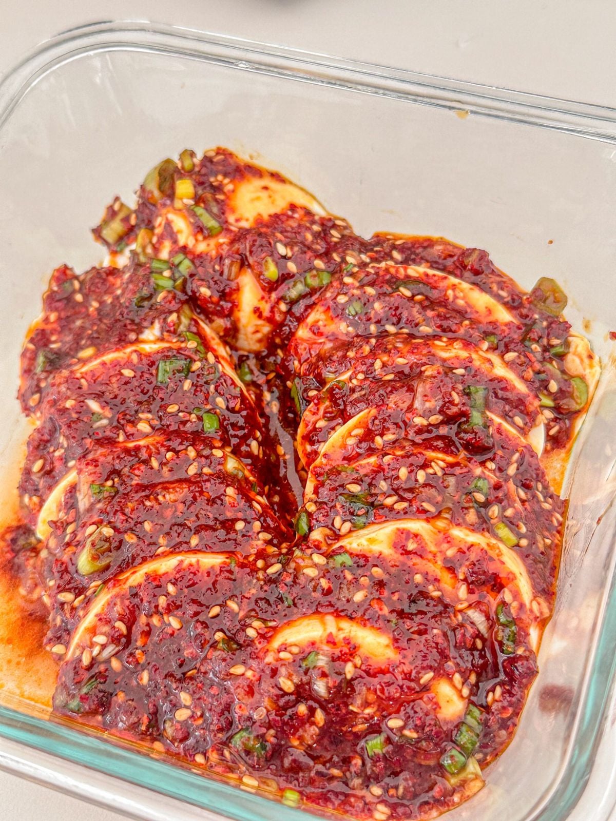 Sliced silken tofu in a spicy, savory Korean sauce with green onions and sesame seeds served in a glass bowl.