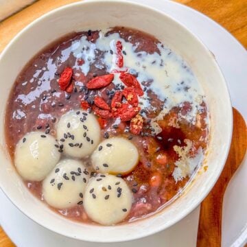 A bowl of red bean soup topped with glutinous rice balls, goji berries, sesame seeds and a light drizzle of milk.
