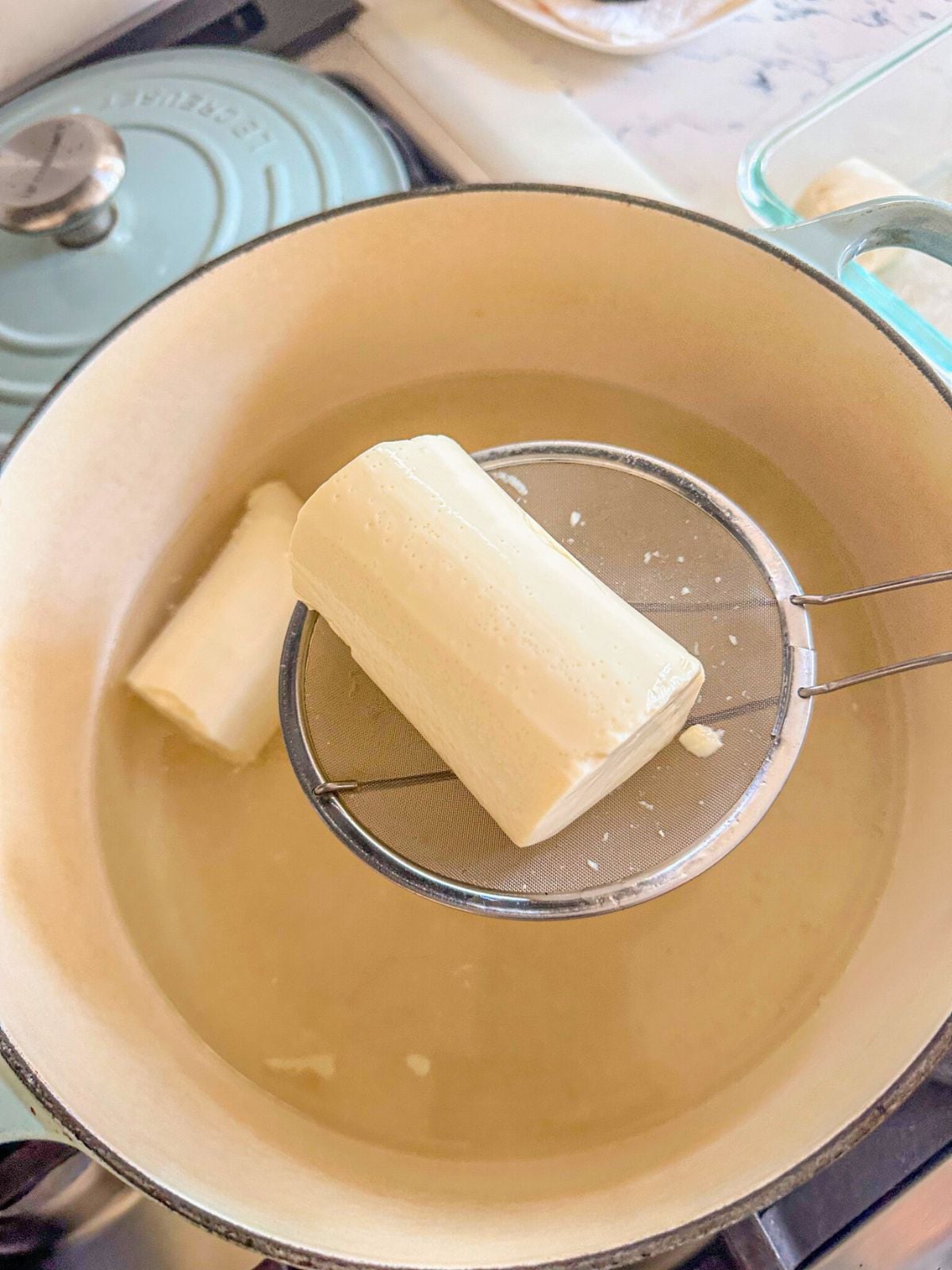 Drained silken tofu on a strainer next to a pot of water with tofu.