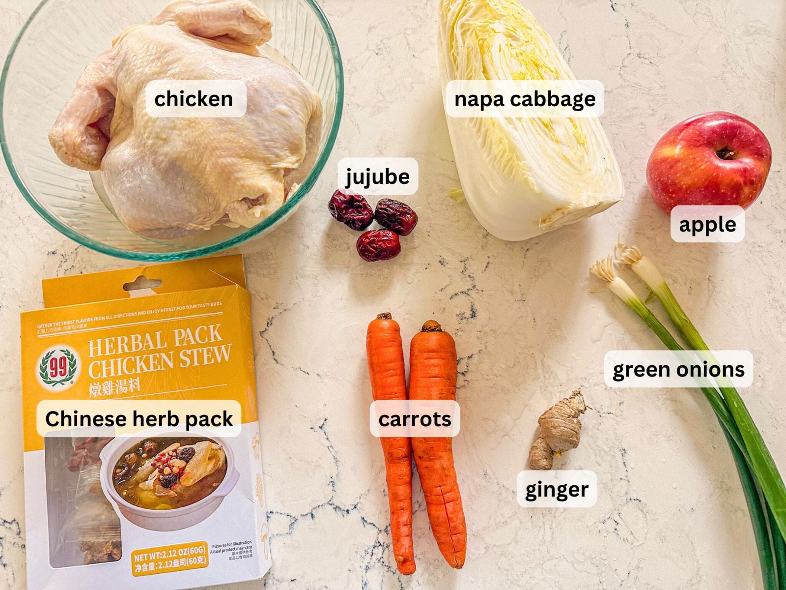 No-water chicken soup ingredients laid out on a table countertop including a whole chicken, cabbage, apple, carrots, jujube, ginger, green onions and Chinese herb pack.