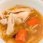 A bowl of soup filled with shredded chicken and chopped carrots.